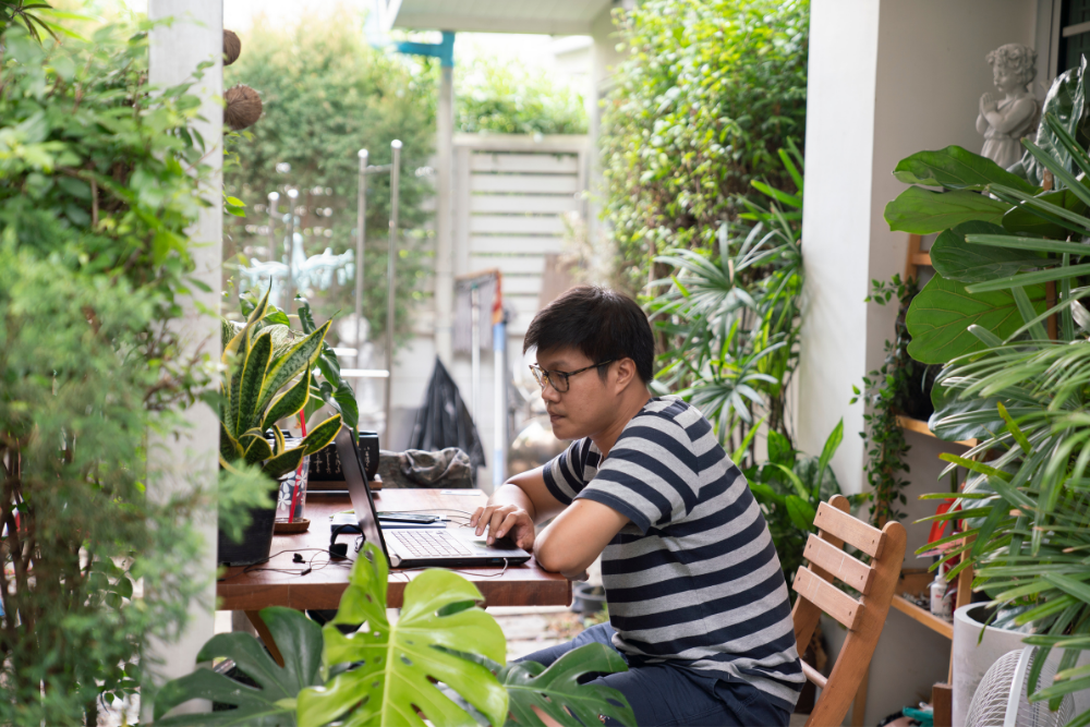 man working on laptop in an outdoor patio surrounded by plants