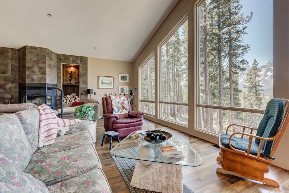 A living room in a luxury cottage with floor to ceiling windows looking over the Rocky Mountains.