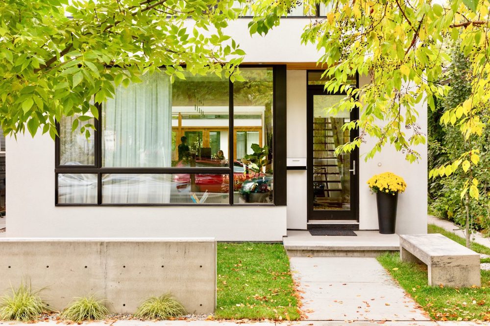 Exterior of a stunning contemporary laneway house in Calgary, featuring a blend of concrete with airy black and white architecture and vivid greenery.