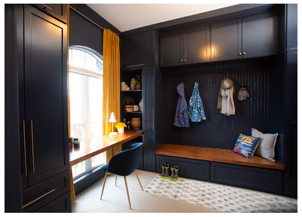 A mudroom and home office with navy blue walls and wood accents