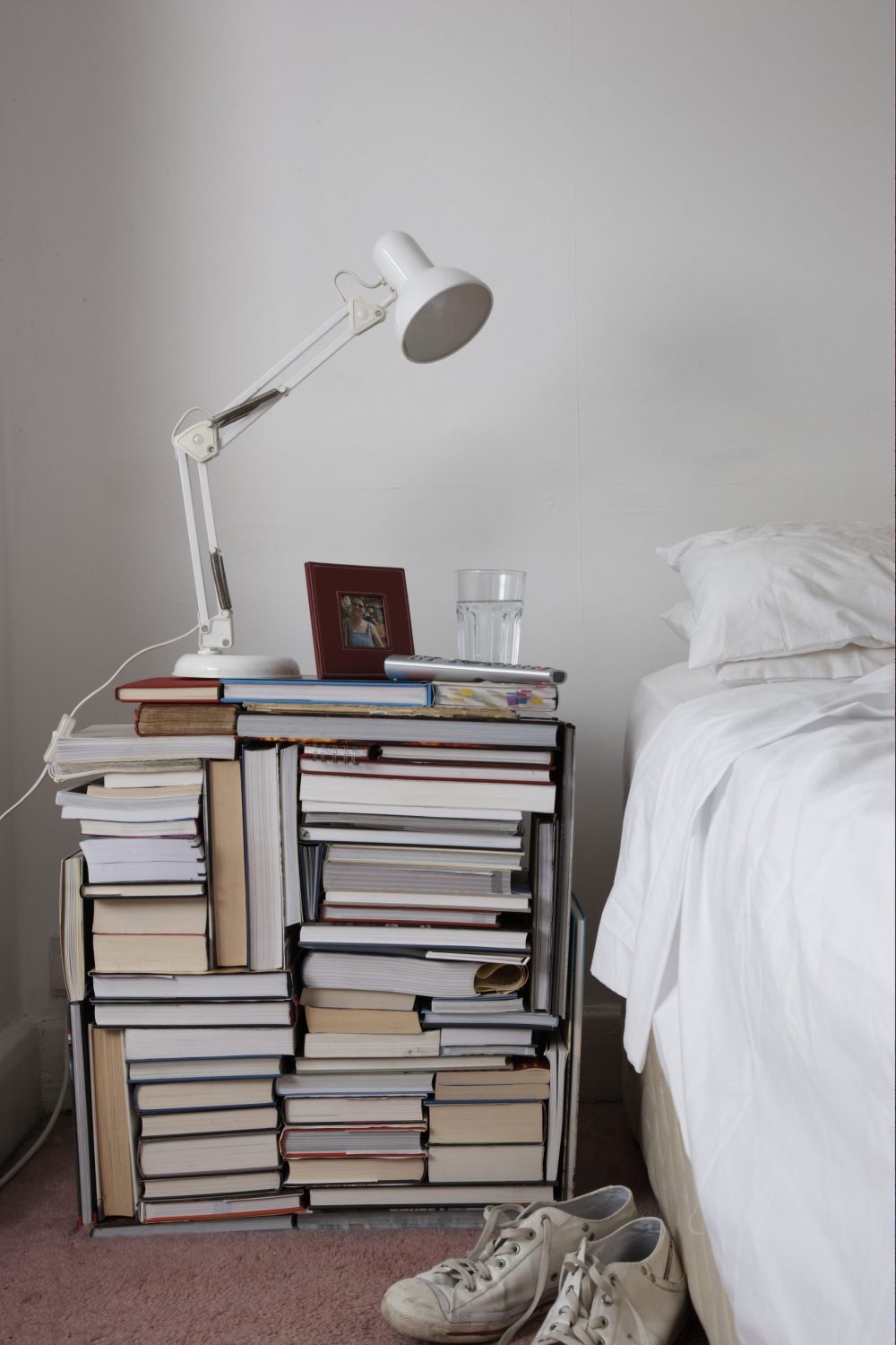 Books of various sizes are stacked together to create a makeshift nightstand.