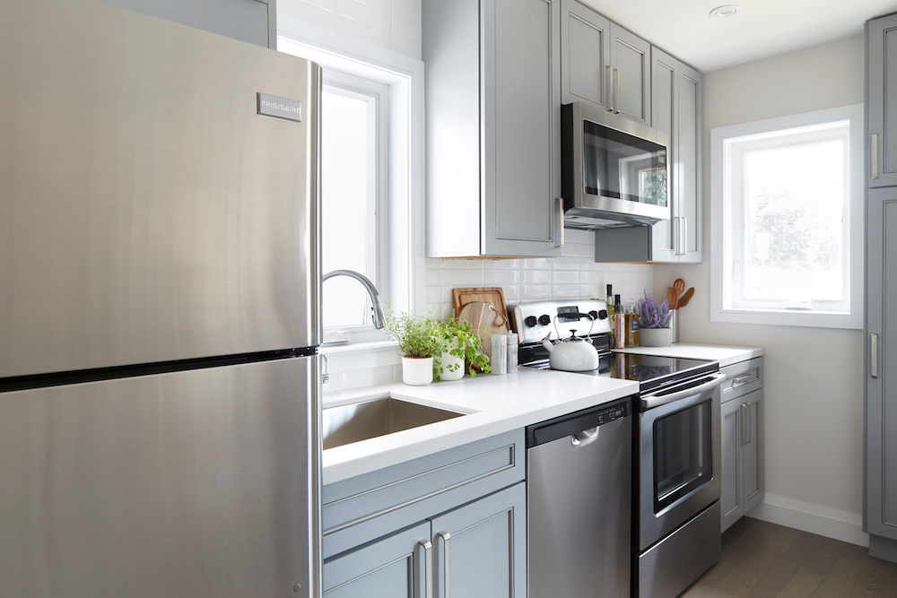 Numerous stainless steel appliances in a small, bright kitchen with white subway tile backsplash and powder blue cabinet with stainless steel hardware.