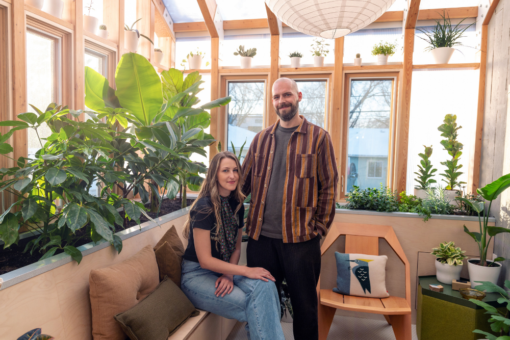 Joe Dort, in a maroon and orange vertically striped button-down, and Tanya Puka, in blue jeans and a black top and neckerchief, pose together in their solarium.