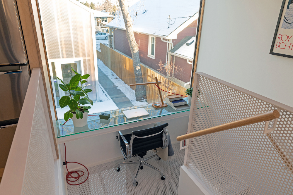 A small home office built into the stair landing, with a glass floating desk against a large window.