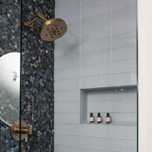 A shower with light blue subway tiles on one wall and a mixture of dark blue penny tiles on the other wall, accented with brass fixtures like the showerhead and tap.