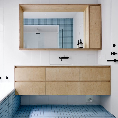 A modern bathroom with white walls, wooden drawers empty of toiletries and knickknacks and a blue tiled floor clear of mats or garbage bins.