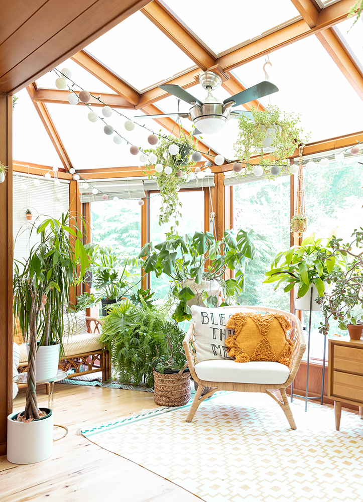 Boho sunroom filled with rattan furniture, geometric rug and lots of plants.