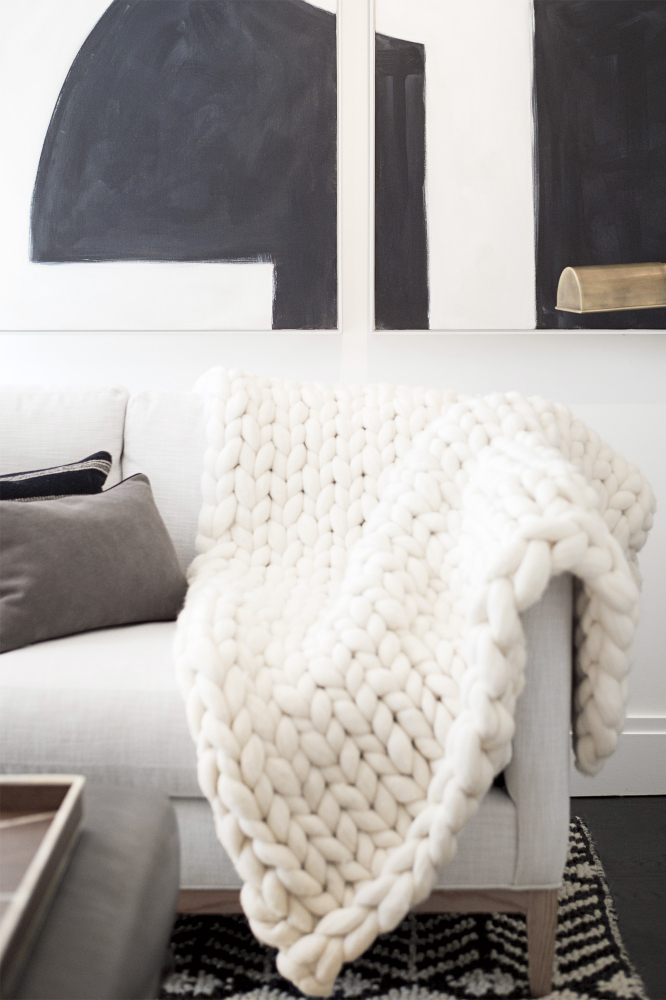 An off-white chunky knit throw blanket is draped over the arm of a grey sofa.