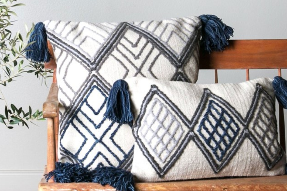 Two white throw pillows with blue embroidery and tassels sit on a rustic wooden bench.