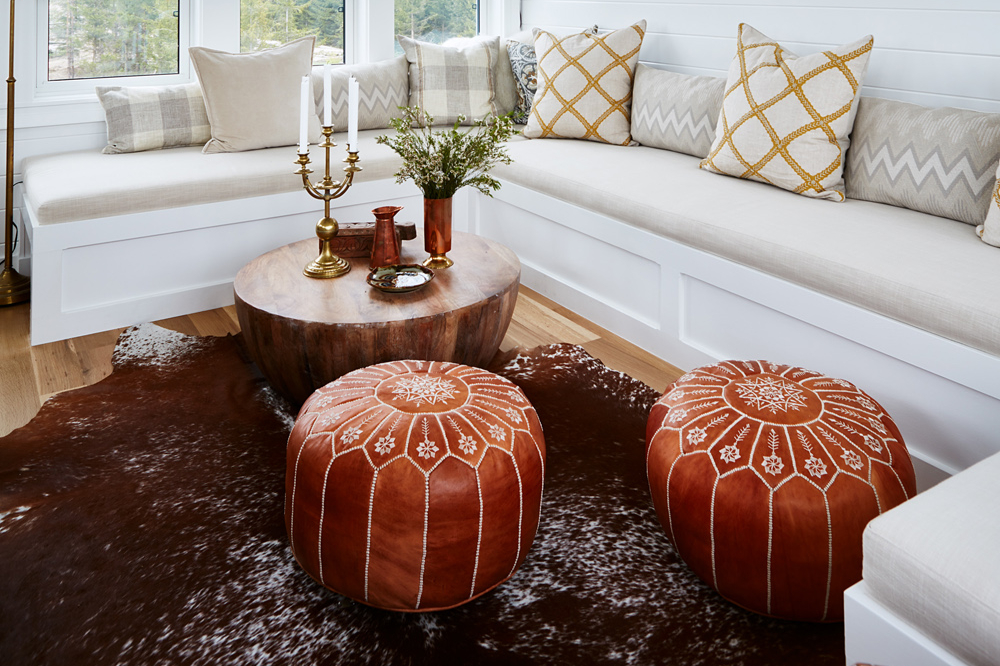A U-shaped custom sofa, round wood coffee table, and two embroidered leather poufs on a faux hide area rug.
