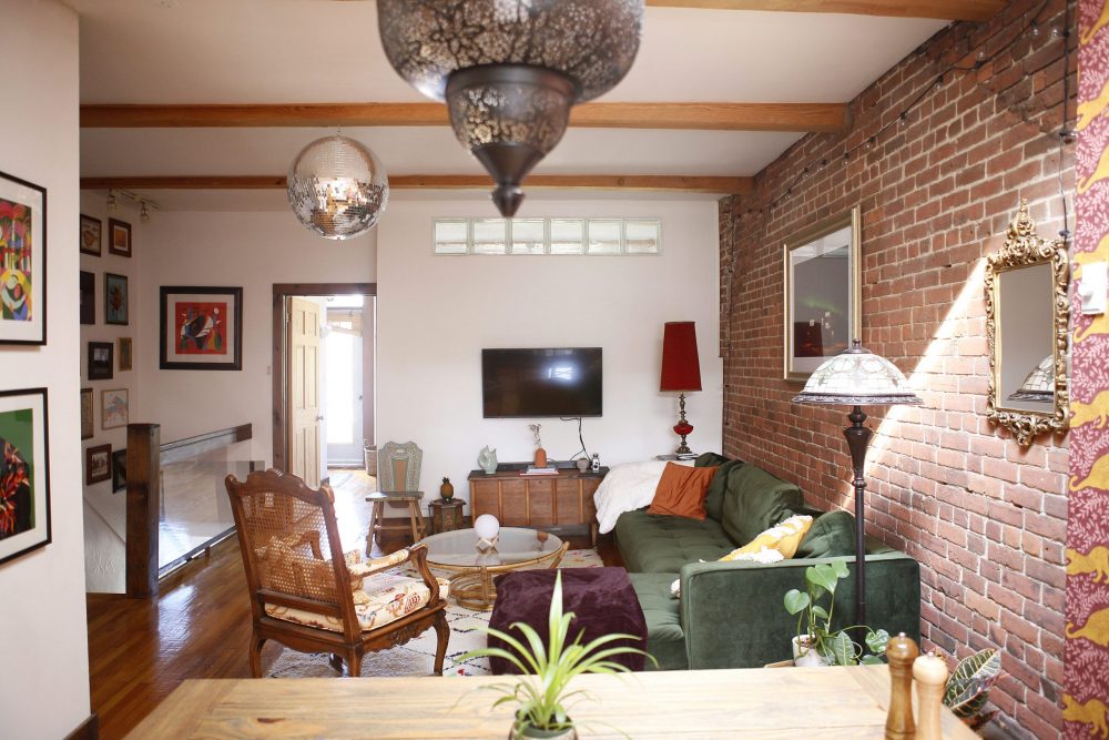 A cozy living room with a green couch, vintage chairs, and a brick accent wall.