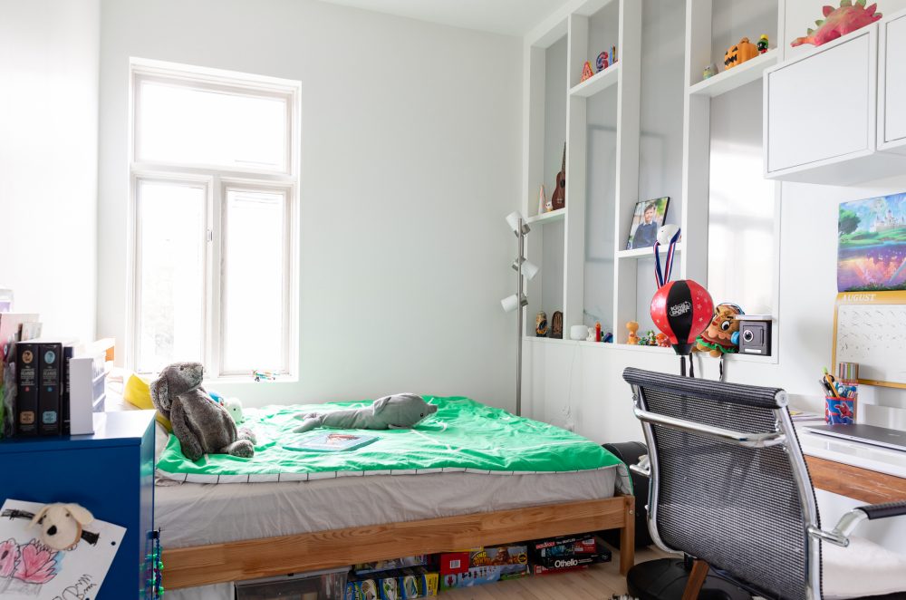 White kids’ room with shelves on wall and green comforter on bed