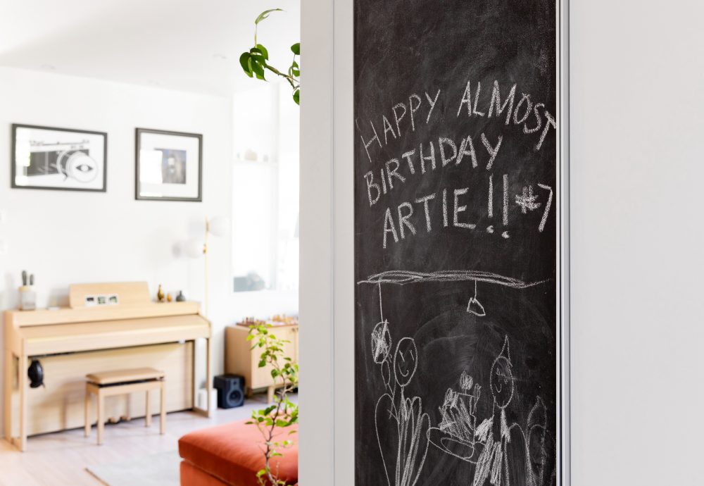 View of chalkboard with “Happy Almost Birthday, Artie!” on it, with a wood piano in the background