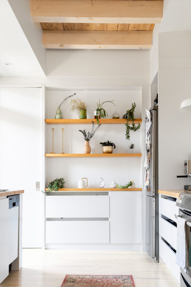 White kitchen with wall of wooden open shelves decorated with an array of green plants and planters