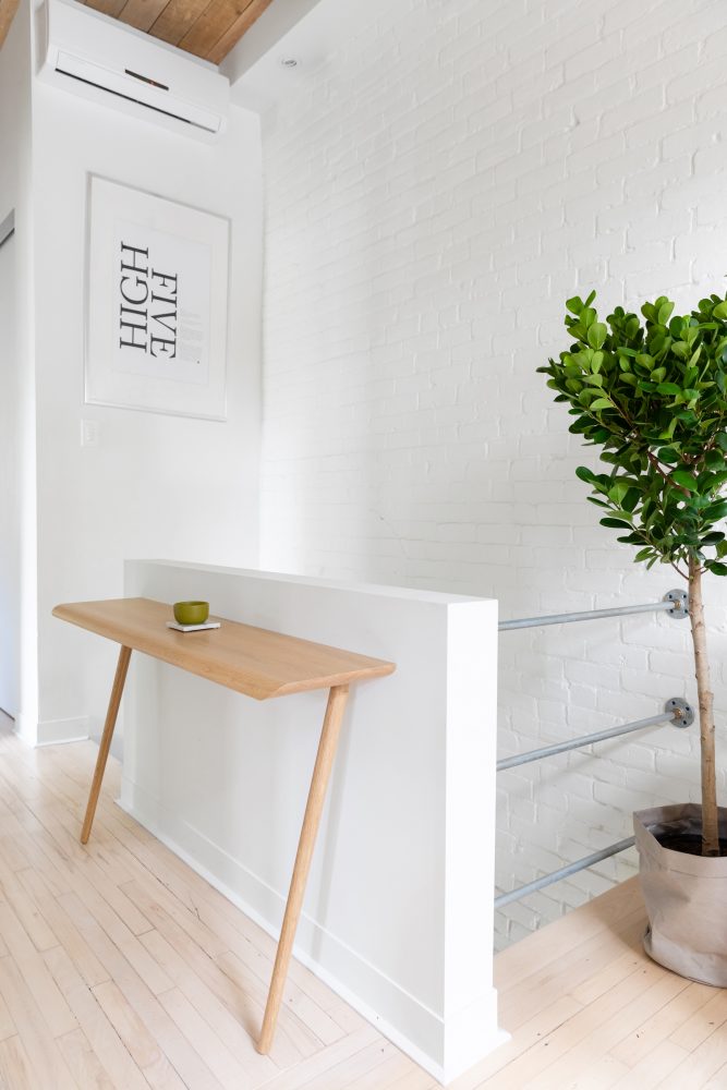 White hallway with white brick wall on one side and a small wooden side table