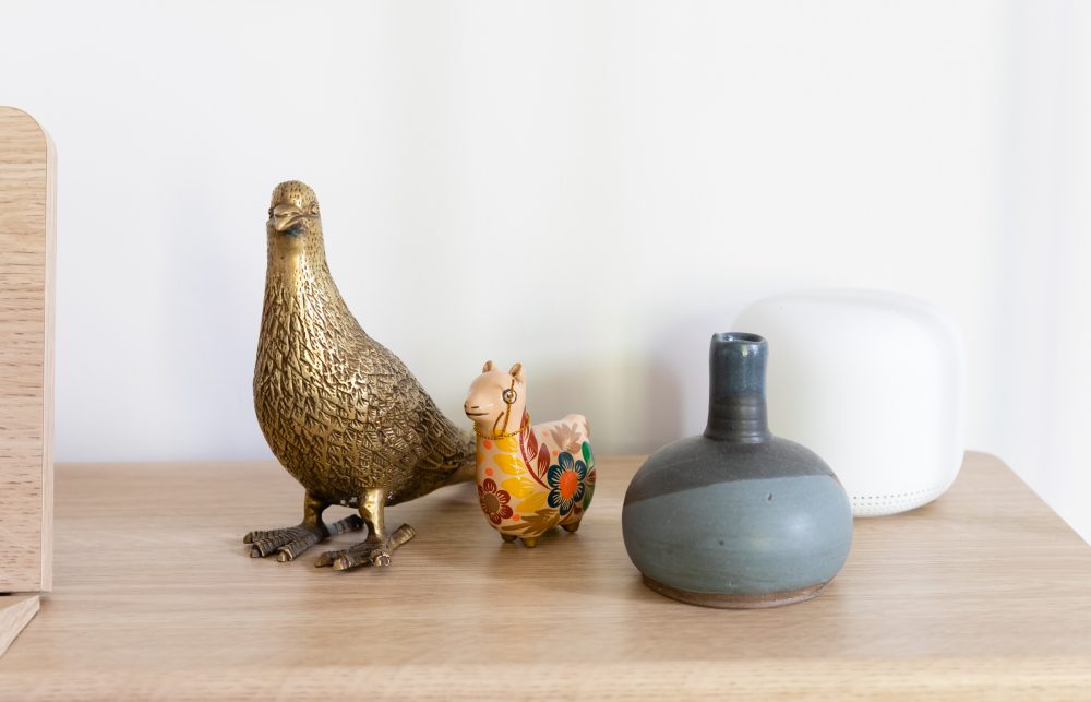 Small array of decorative ornaments like a metallic bird and small blue vase on top of wooden piano
