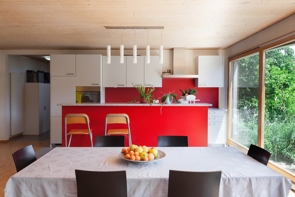 A vibrant kitchen with red backsplash, a red island, granite countertops and white cabinetry.