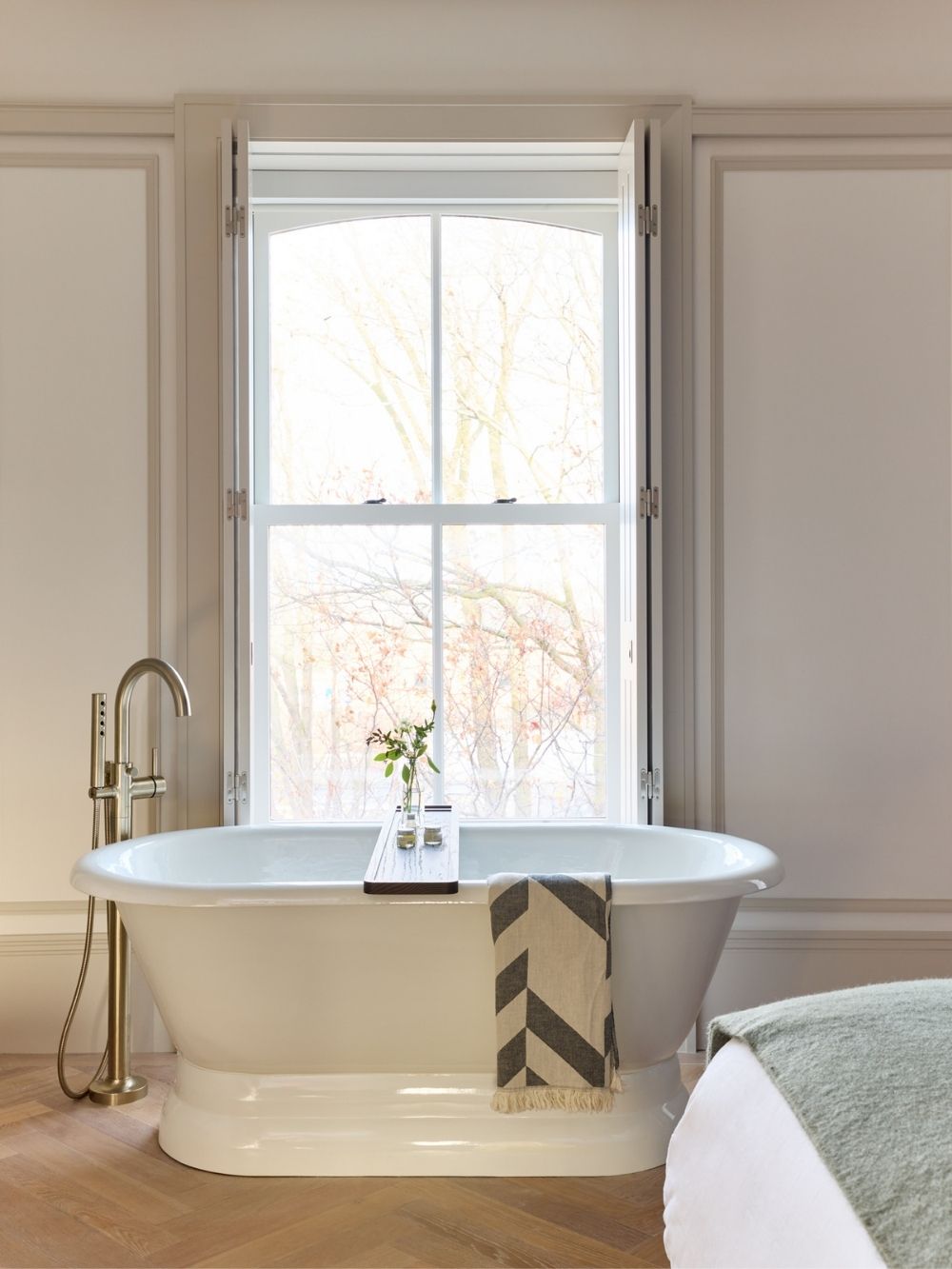 soaker tub in front of window, grey and white tasseled throw over the side