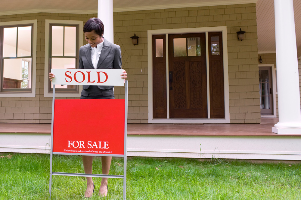Real estate agent putting a sold sign up in front of a sold home