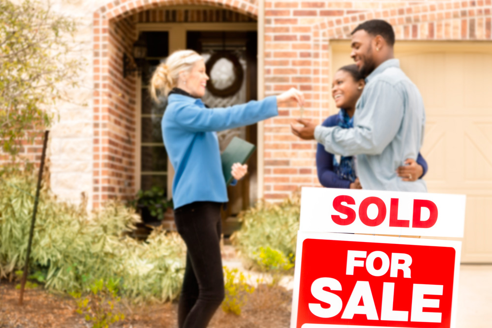 Realtor and clients in front of a sold sign