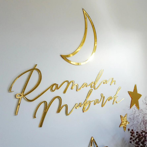 Gold wall hangings spelling out Ramadan Mubarak, along with a crescent moon shape and stars.
