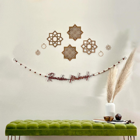 A wall-hanging reading Ramadan along with several geometric decor pieces, hanging above the green bench.