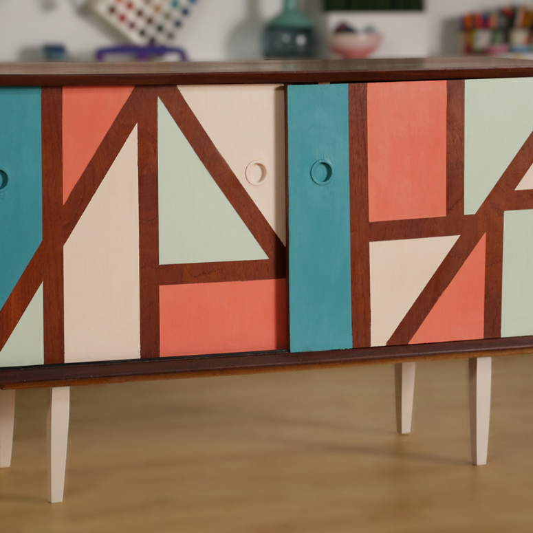Upcycle Your Old Credenza: A wooden credenza with geometric patterns painted on its front in pastel colours, and its four wooden legs painted cream.