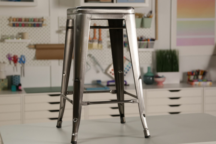 A four-legged silver metal stool atop a workbench.