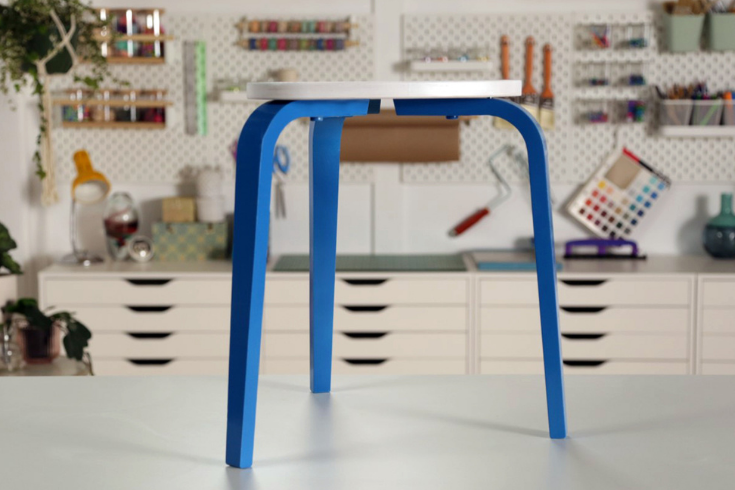 The three-legged wooden stool spraypainted blue on its legs and a creamy white on its seat.