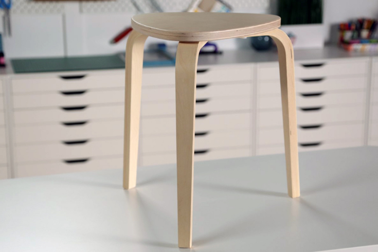A plain wooden 3-legged stool atop a workbench.