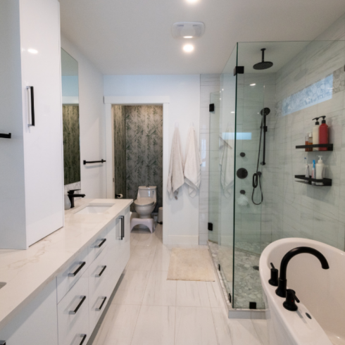 white bathroom with black hardware, tub on right in front of glassed in shower
