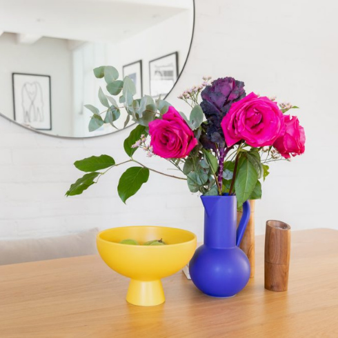 Pink flowers in bright blue vase on wooden dining room table