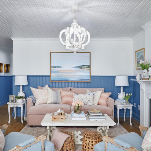 A living room with blue wainscoting, a blush pink sofa and seaside inspired artwork