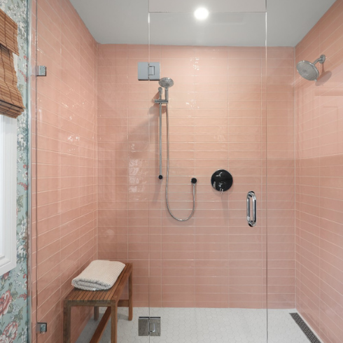 A spacious walk-in shower with peach pink subway tile and glass door