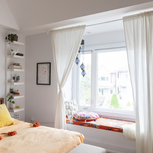 window seat in white bedroom with long, airy white curtains at the window
