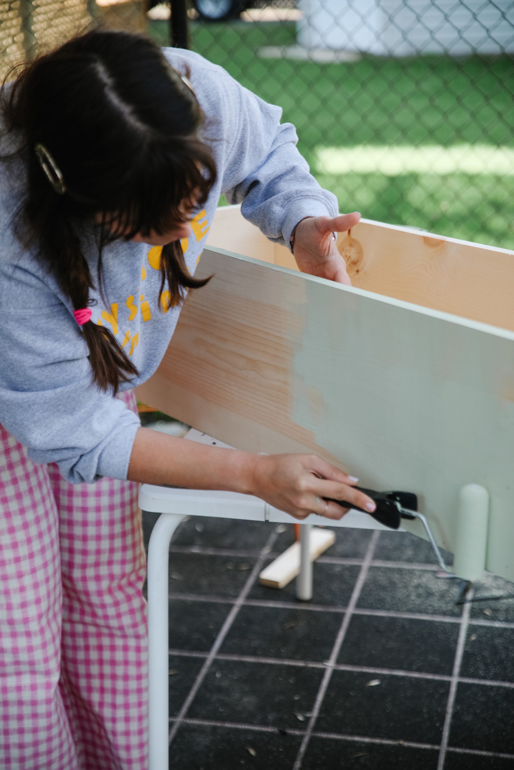 Maca using a paint roller to paint the exterior of her DIY planter box.