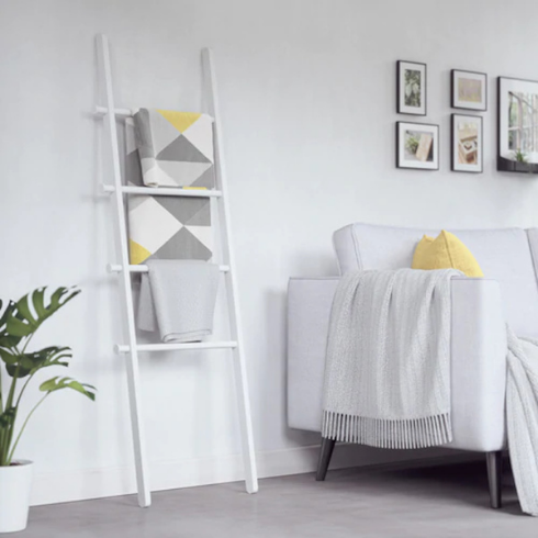 A white living room with a white couch, white walls, a white Umbra Hub Ladder with three blankets, and a grey floor
