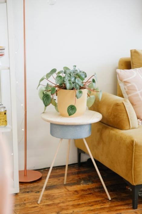 The three-legged DIY planter stand sits next to a yellow sofa.