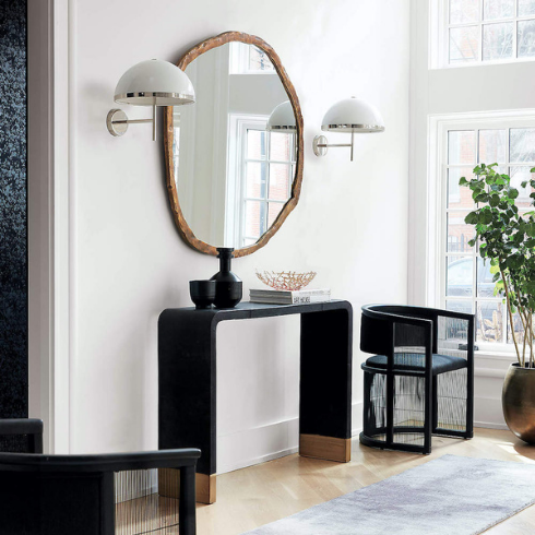 Chic living room with a CB2 Abel Brass Round Wall Mirror hangs on the white wall, two white sconces, a black occasional table standing below it and a black chair