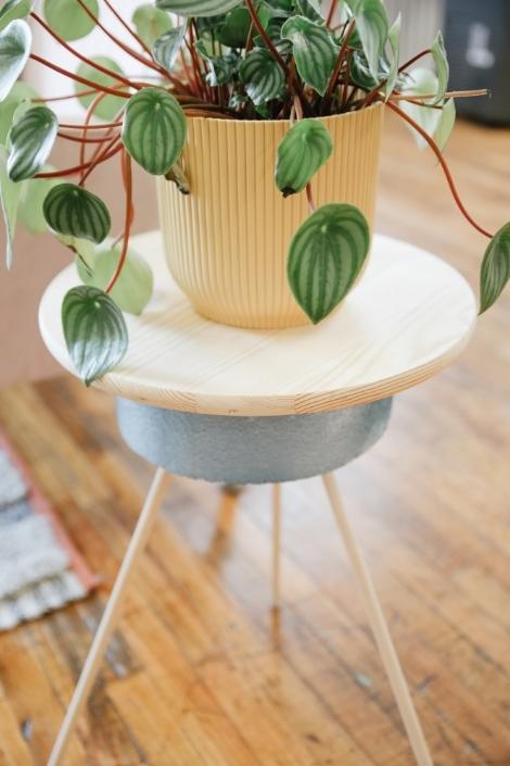 A closeup of the DIY planter stand, with a plant sitting atop it in a ribbed yellow pot.