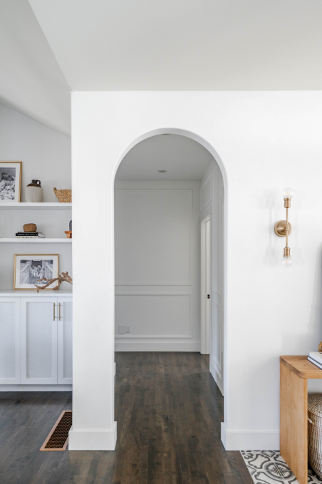 An arched doorway leads into a white corridor. A brass wall sconce is situated beside the arch.