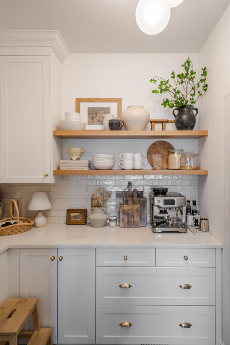 Two wooden open kitchen shelves are styled with white ceramic dinnerware, wood and natural ceramic decor and fresh greenery.