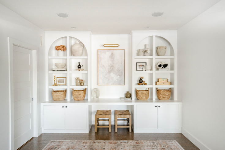 Large white arched shelves and white lower cabinetry flank a little built-in desk area. A large abstract painting hangs in the middle, above the built-in desk and between the two shelves on either side.