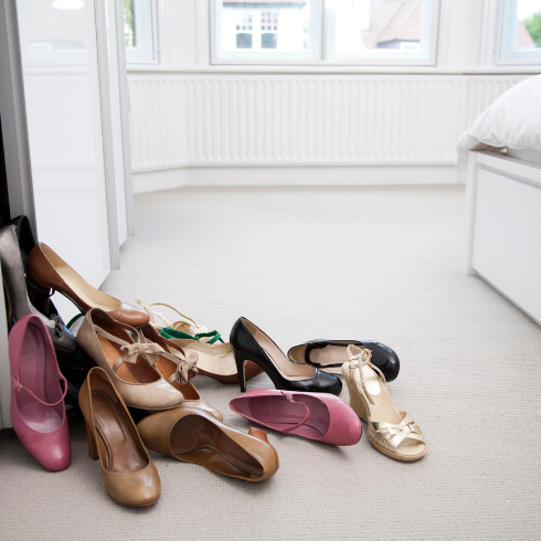 A pile of shoes falling out of a closet and onto the floor of a bedroom.