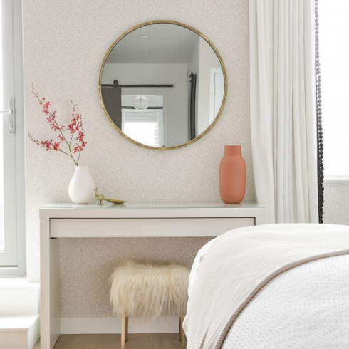 A round mirror hangs above a dresser in a beige room.