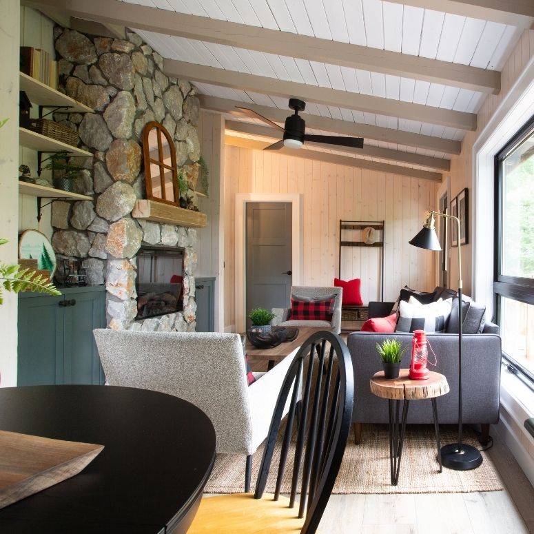 Living room with stone fireplace, black kitchen table and three grey sofas