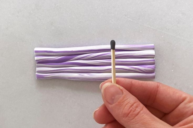 A person holding a match in front of a purple clay block 