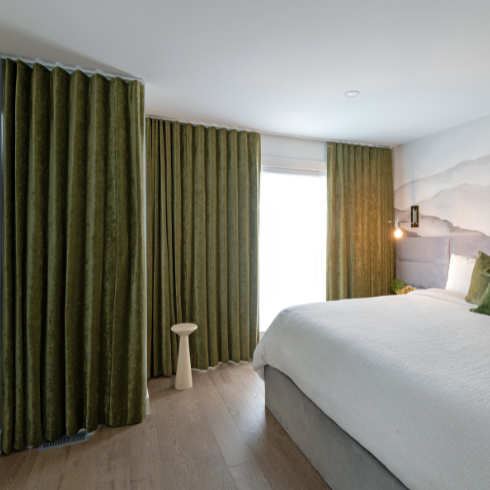 Long, dark green drapes achieve the clean aesthetic, hanging from ceiling to floor across an entire side of the bedroom.