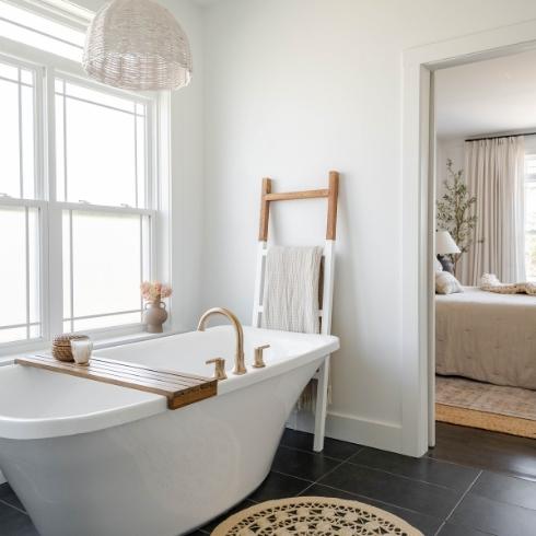 A bathroom with a big white tub, wooden towel rack and linen towels