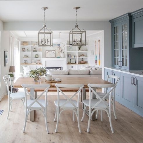 A kitchen with blue cabinets, white dining room chairs and a wooden dining table
